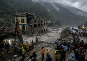 Rescue workers and onlookers gather beside a collapsed building and raging muddy flood in a misty mountain valley