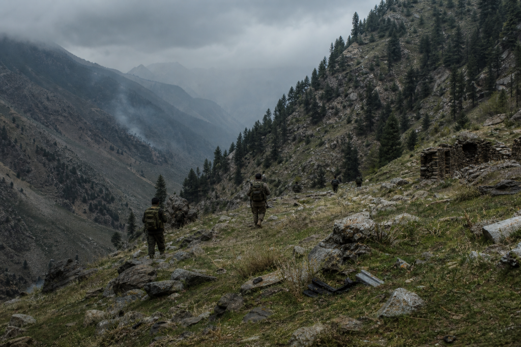 Soldiers hike along a rocky mountain trail beneath a cloudy sky