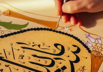 Close-up of hand painting Arabic calligraphy with intricate details.